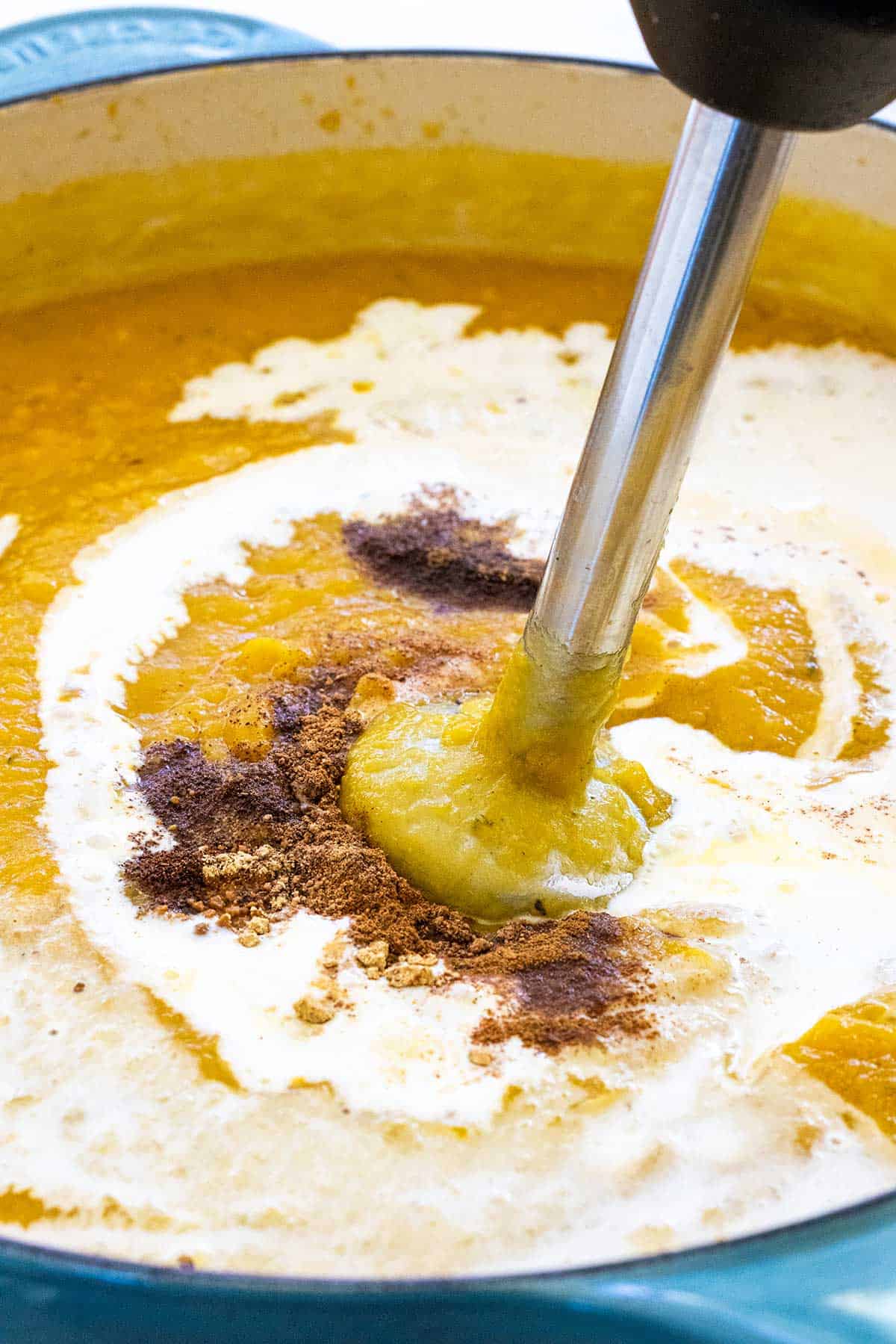 Handheld stick blender mixing a soup.
