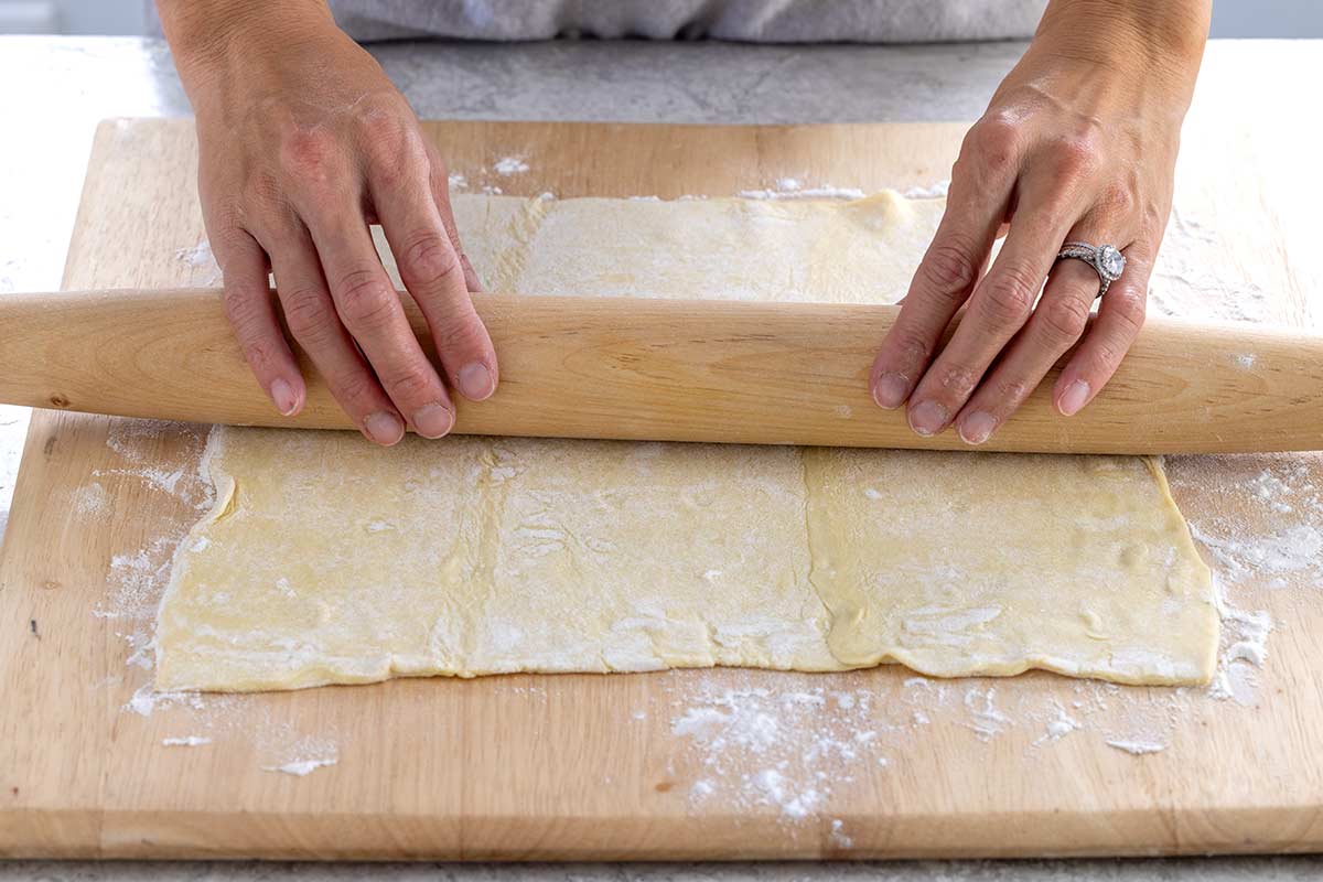 Person rolling out puff pastry on a floured cutting board.