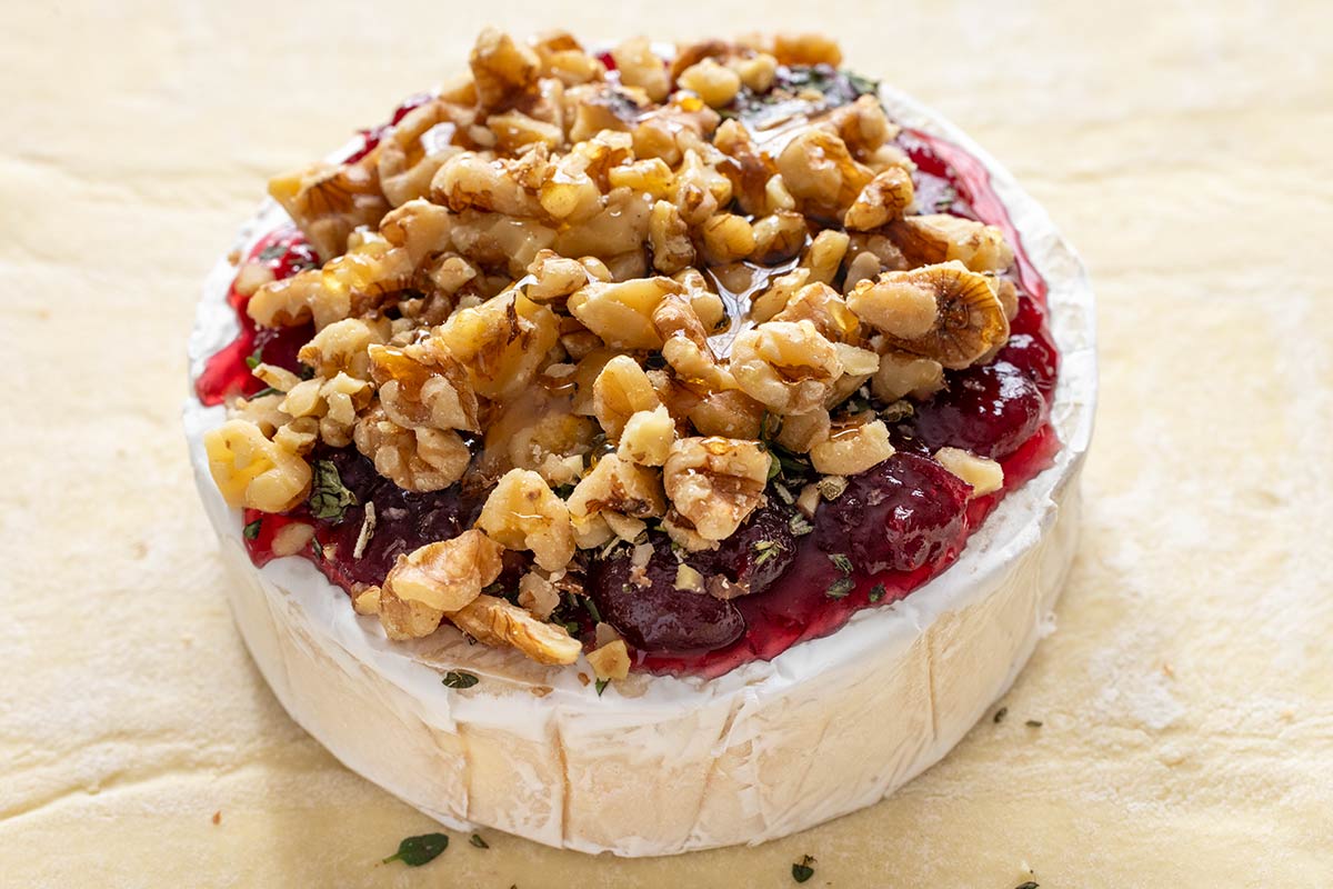 Brie cheese wheel with cranberry sauce, chopped nuts, and honey on top.