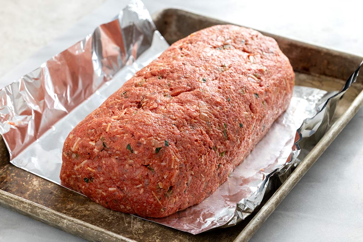 Raw meatloaf mixture shaped into a rectangular loaf resting on an aluminum foil sling.
