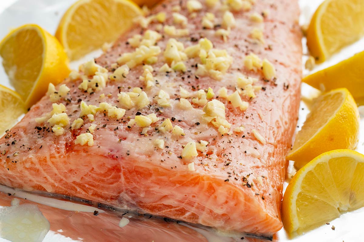 Close up photo of crushed garlic pieces on top of a salmon fillet.