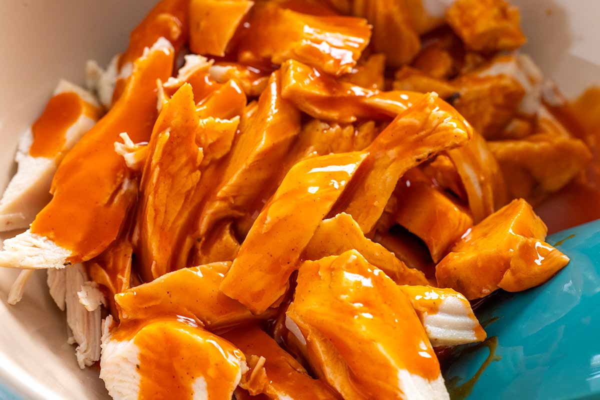 Bowl of shredded chicken coated with hot sauce on top.