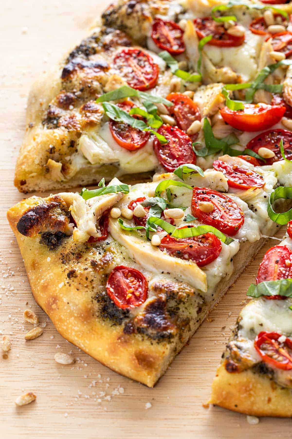 Chicken pesto pizza cut into slices on a wooden cutting board.