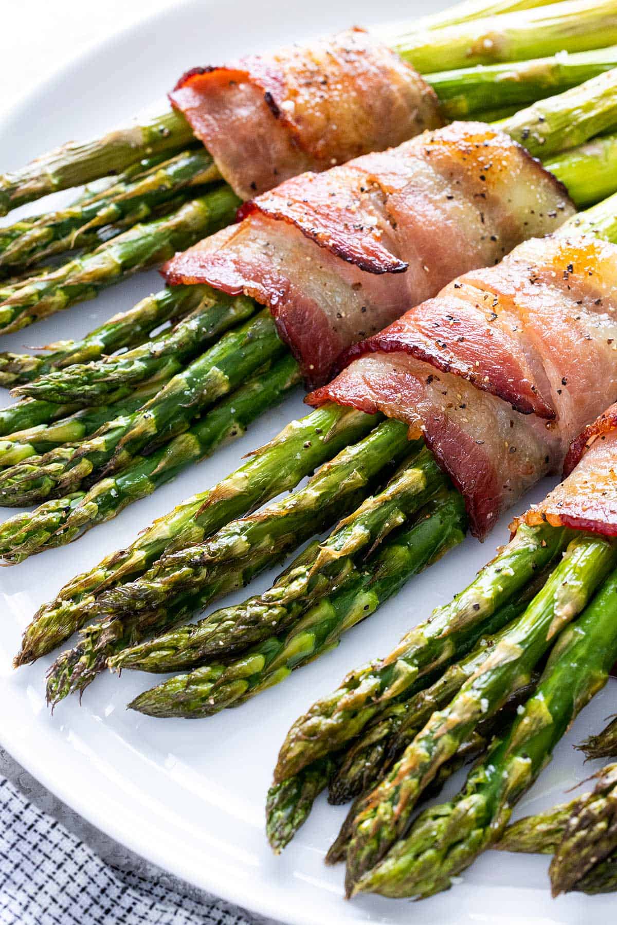 Roasted bacon wrapped asparagus on a white platter.
