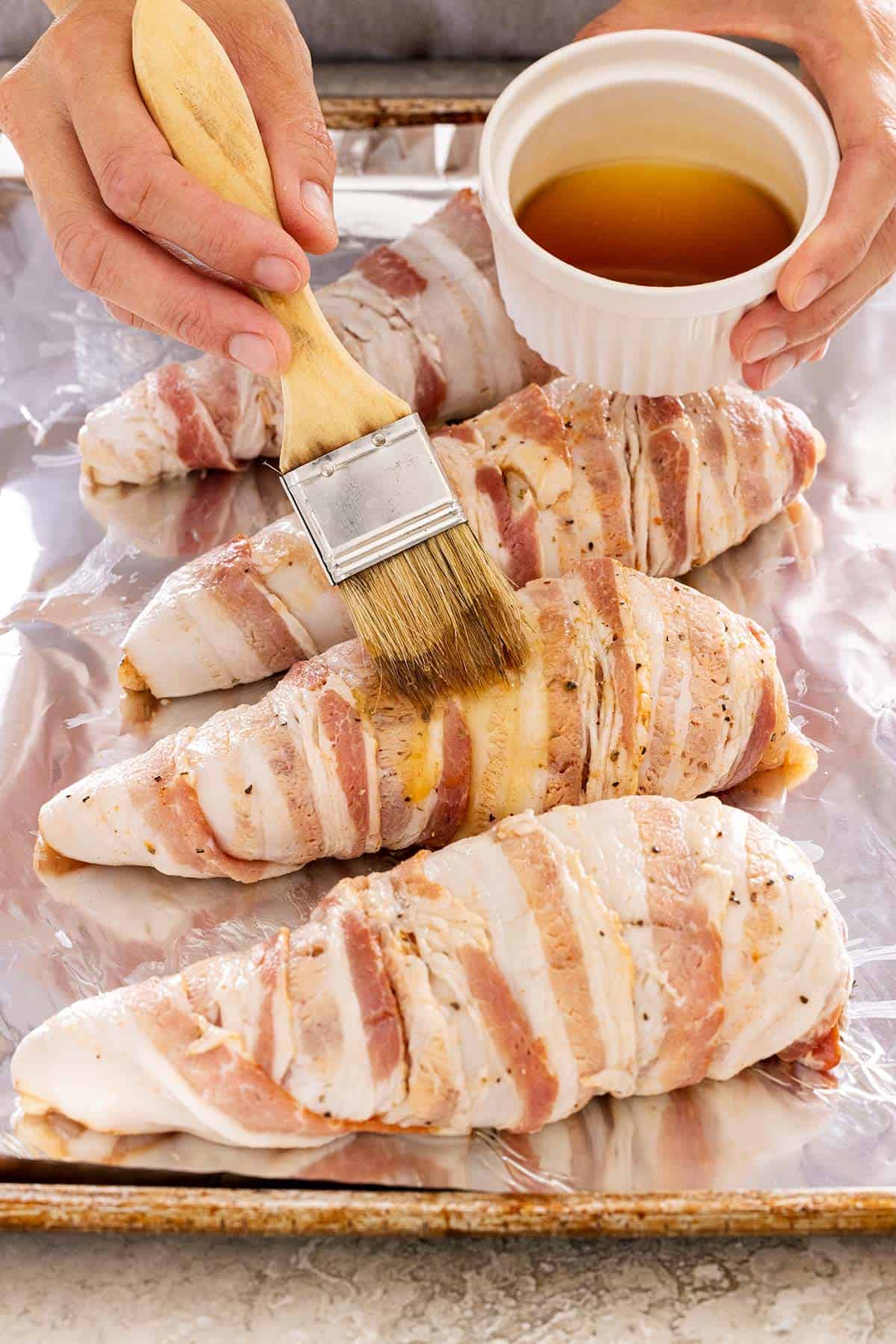 Brushing maple syrup over bacon wrapped chicken breasts.