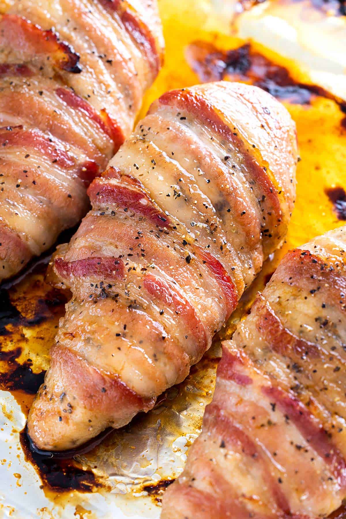Bacon wrapped chicken pieces on a roasting pan.