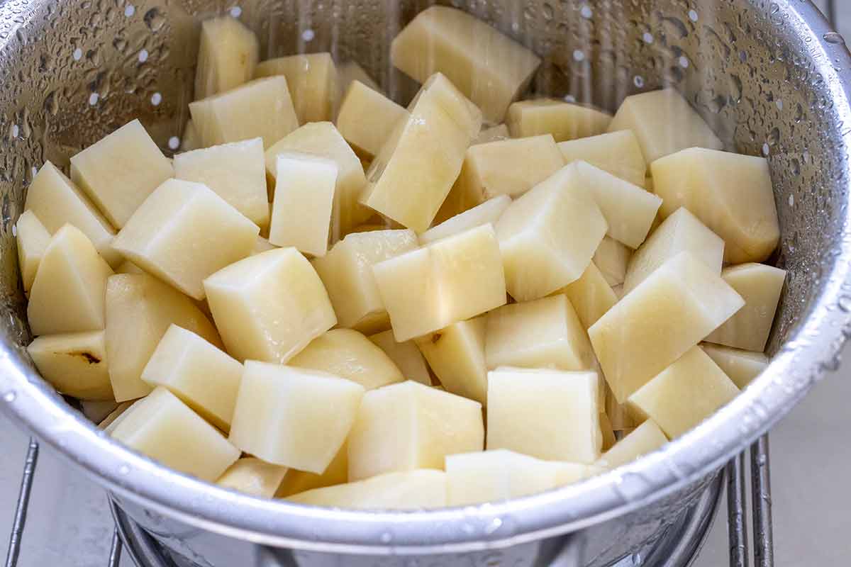 Cubes of potatoes in a colander being rinsed with water.