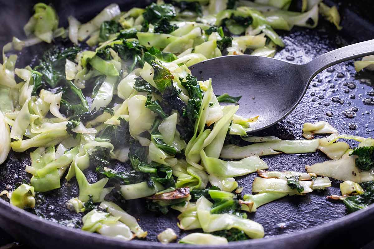 Kale and cabbage sauteing in a cast iron skillet.