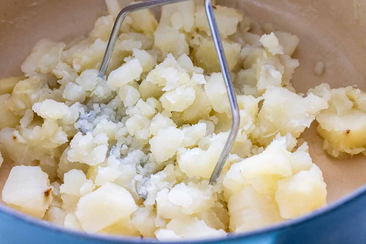 Potato mashed being used on cubes of cooked potatoes in a pot.