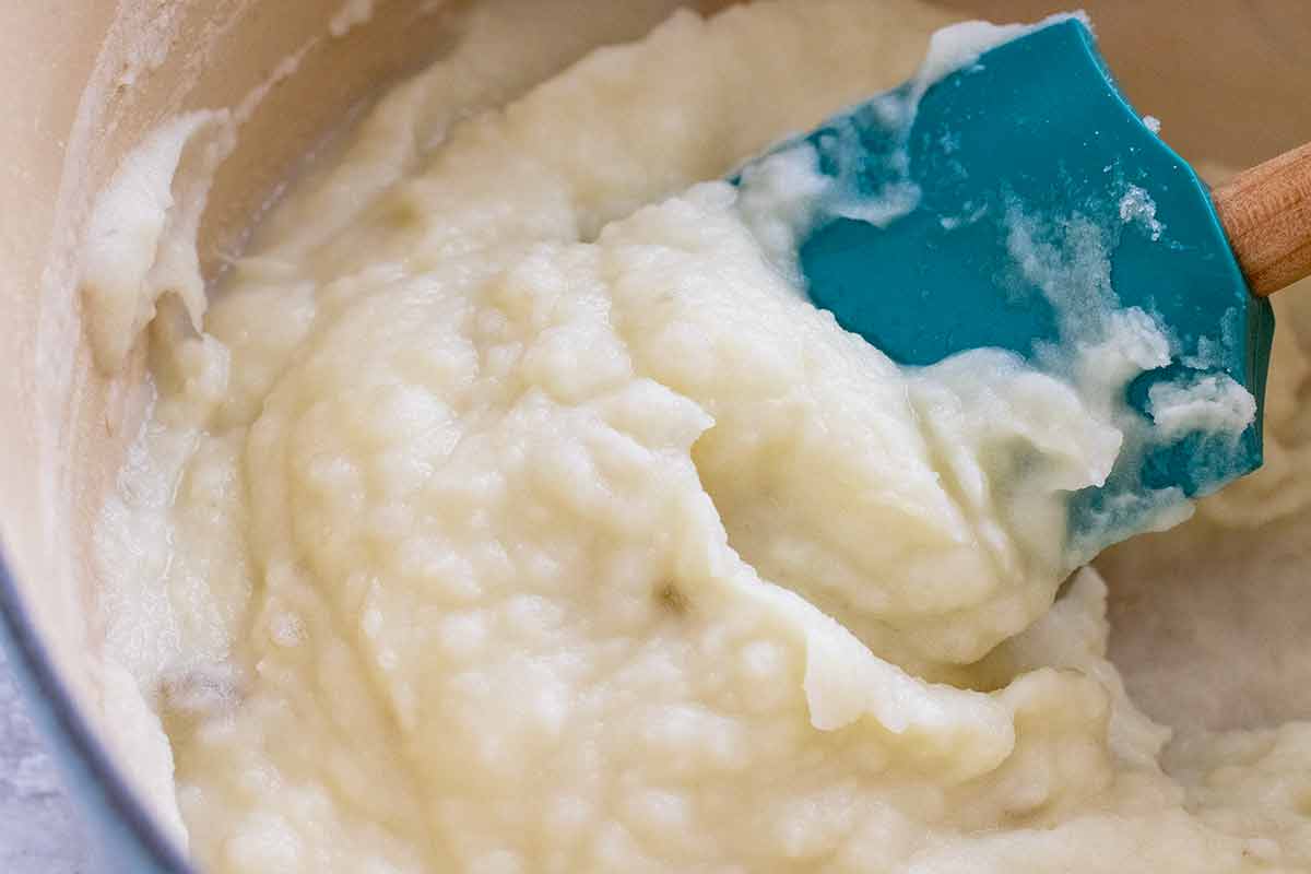 Spatula mixing warm milk into a pot of mashed potatoes.