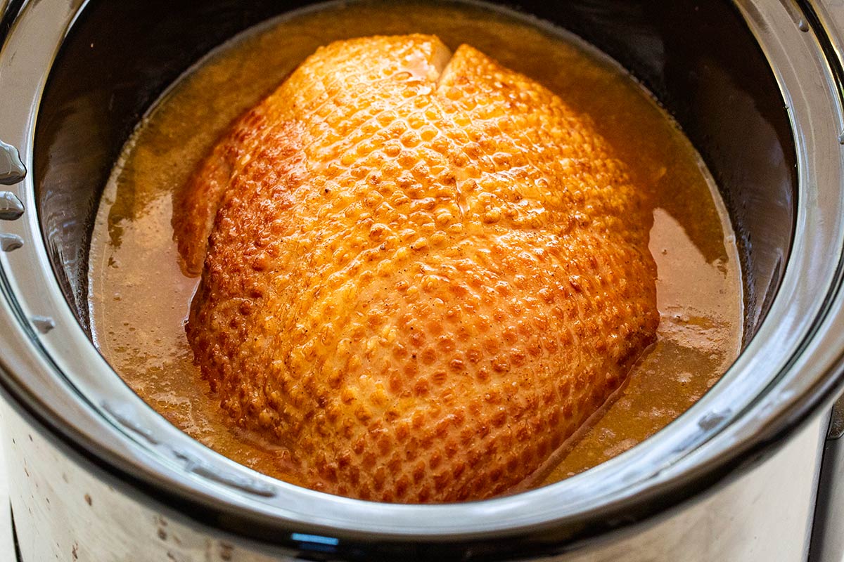 Large ham cooking inside a slow cooker.