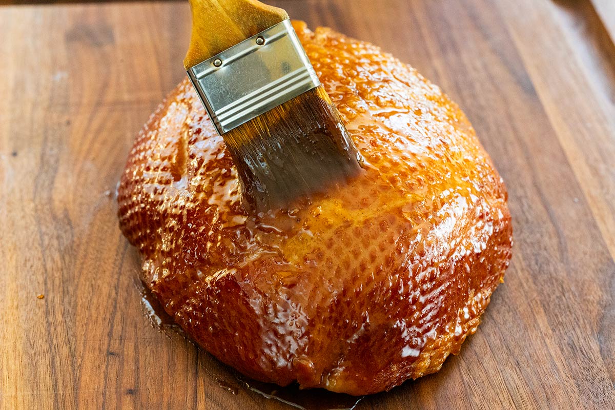 Brush basting brown sugar glaze on the outside of a ham.