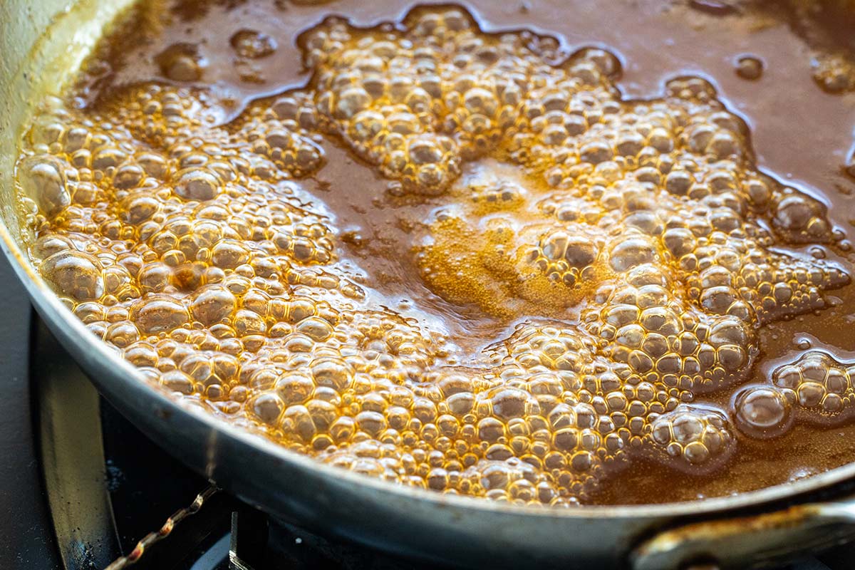 Bubbles forming on a brown sugar glaze being cooked in a saute pan.