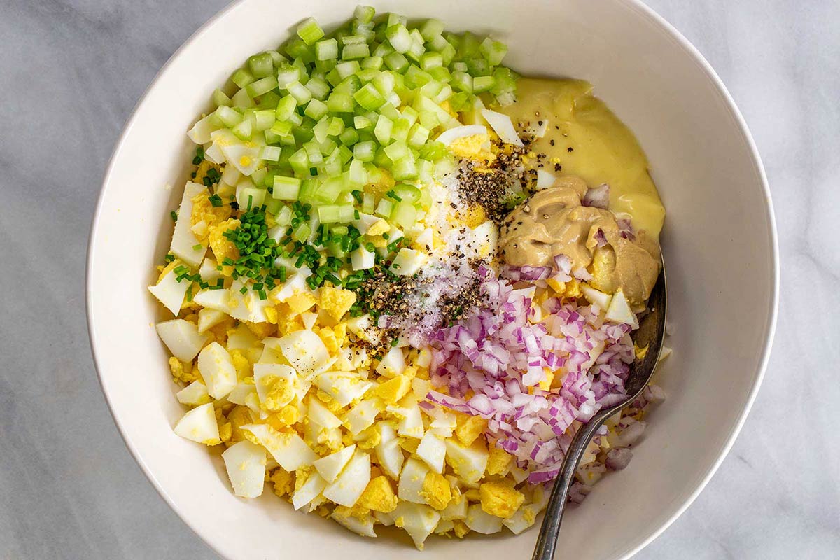Eggs, onions, celery, other ingredients in a bowl ready to be mixed.