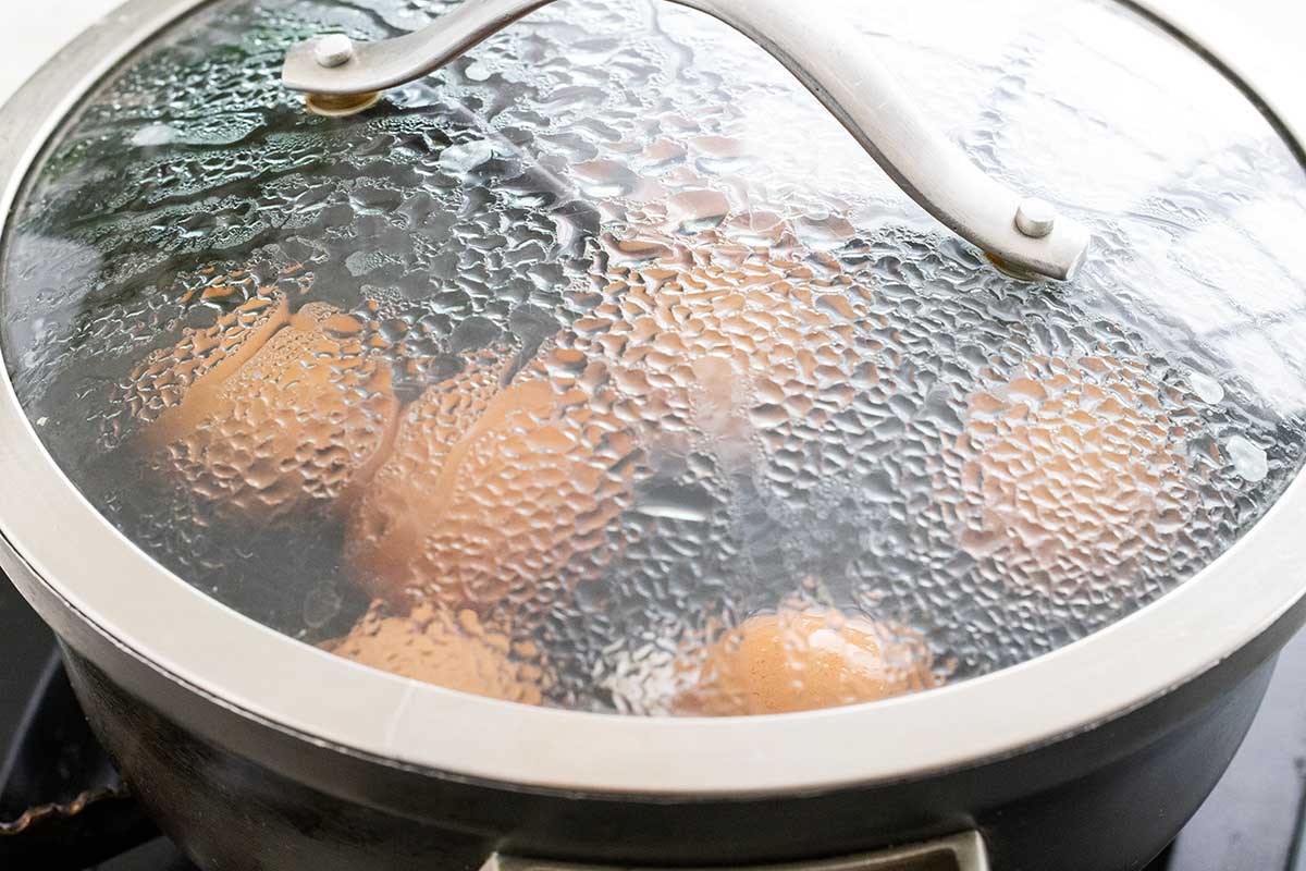 Eggs being boiled in a saucepan with a glass lid.