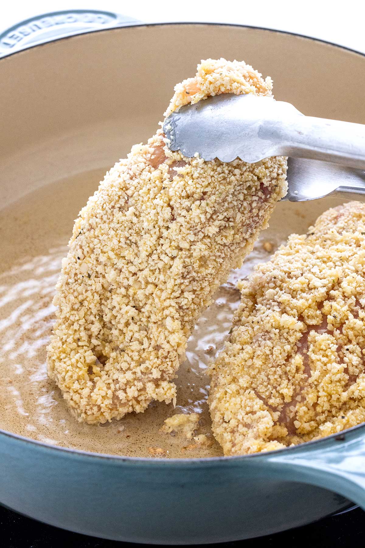 Stuffed chicken breast covered in bread crumbs and about to pan fry in oil.