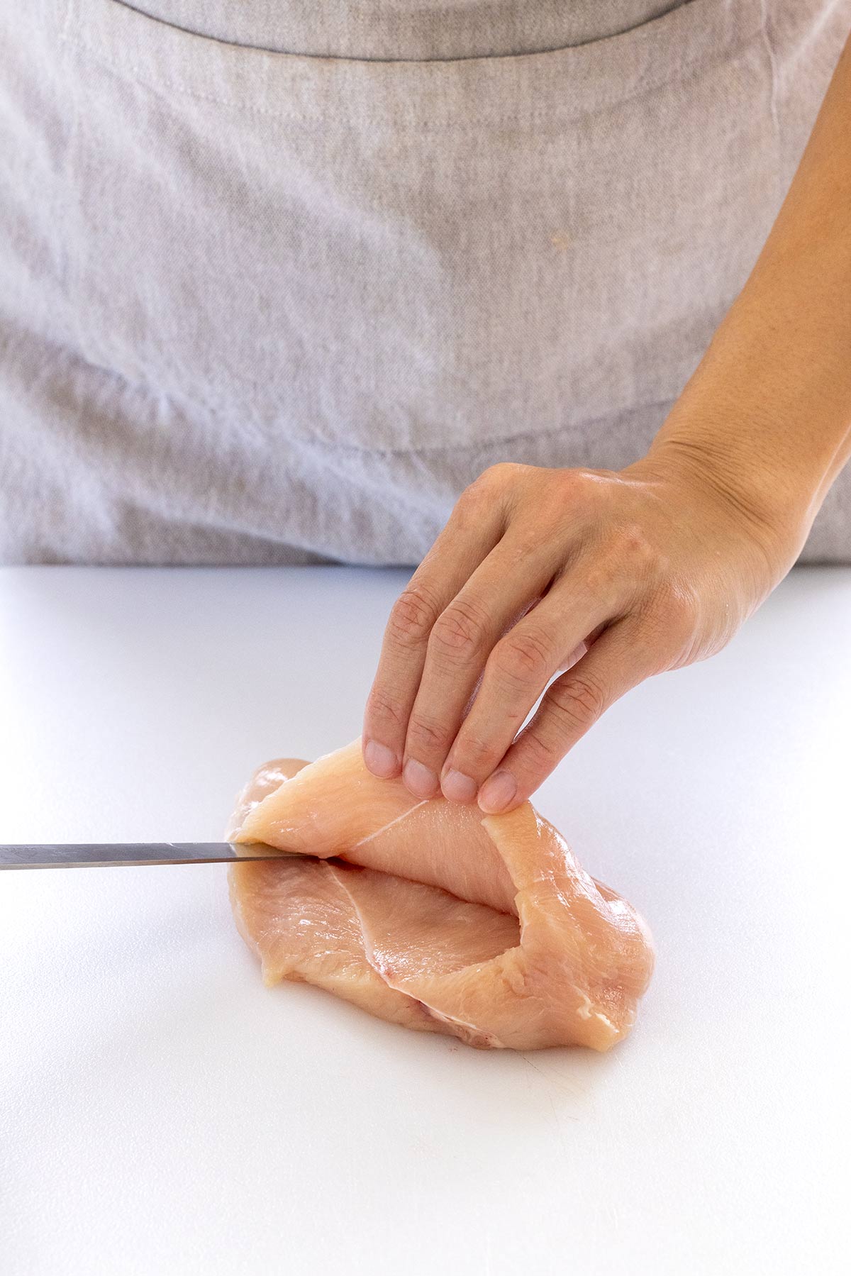Person cutting a slit into the side of a chicken breast.