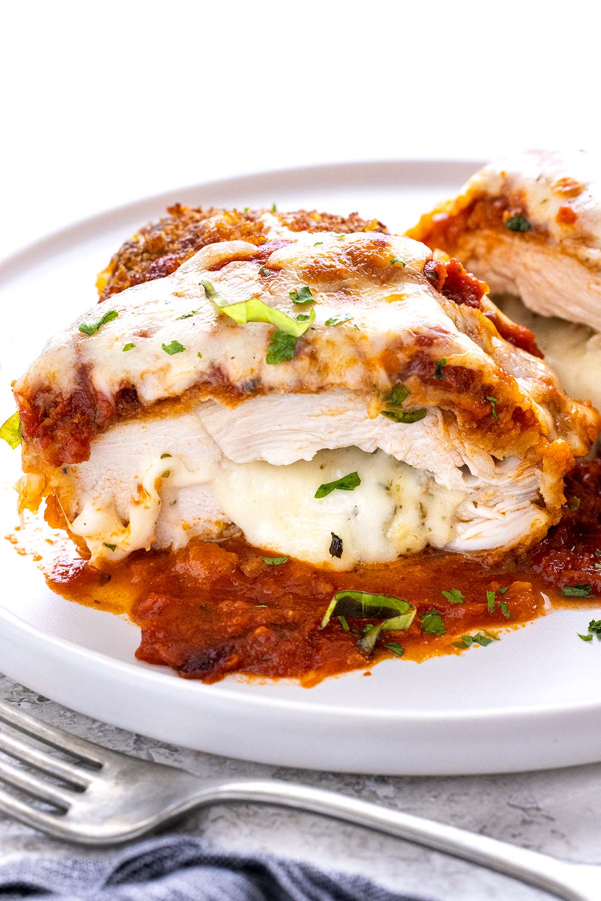 Stuffed chicken parmesan cut in half and served on a white plate.