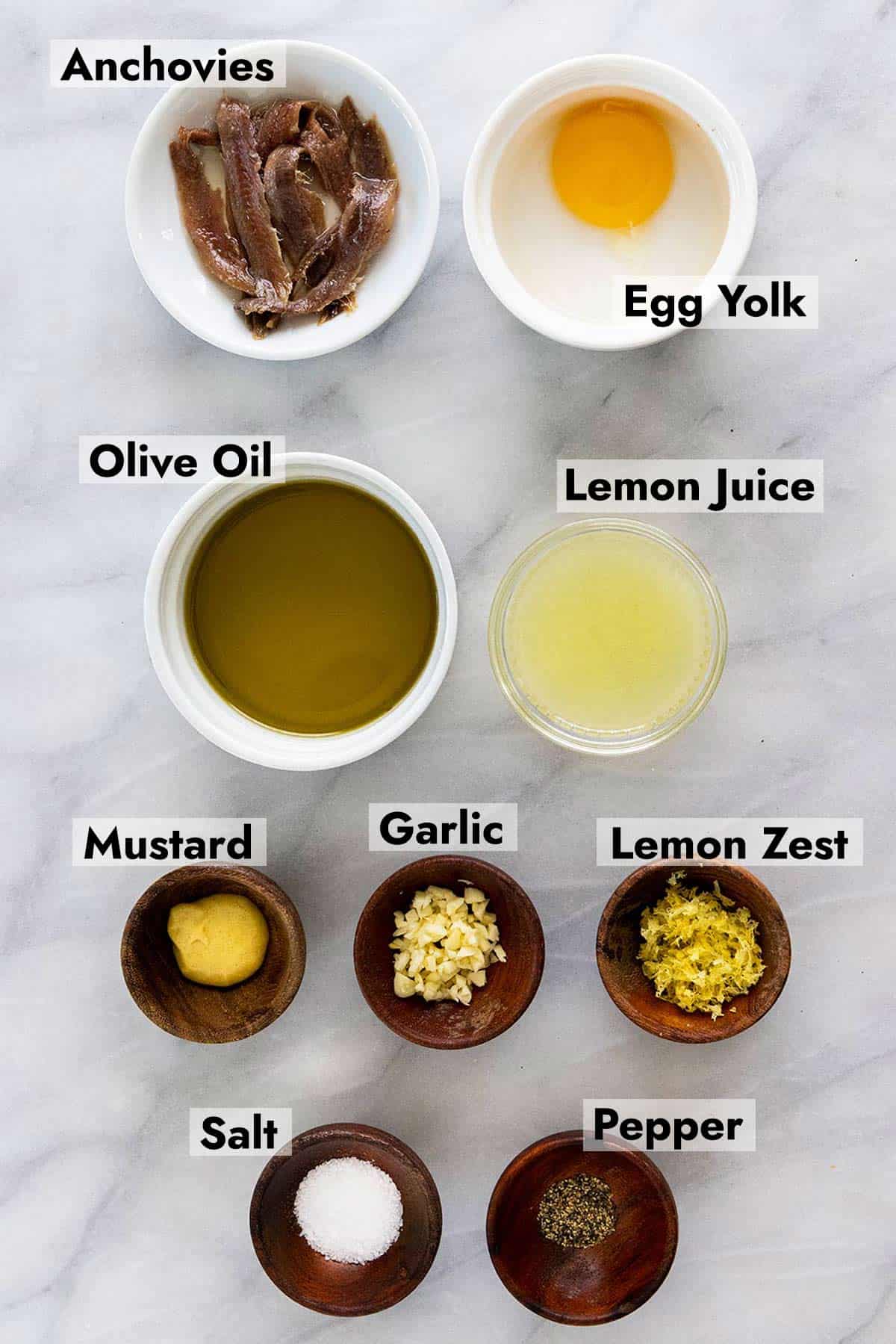 Ingredients in portioned little bowls to make a caesar salad dressing.