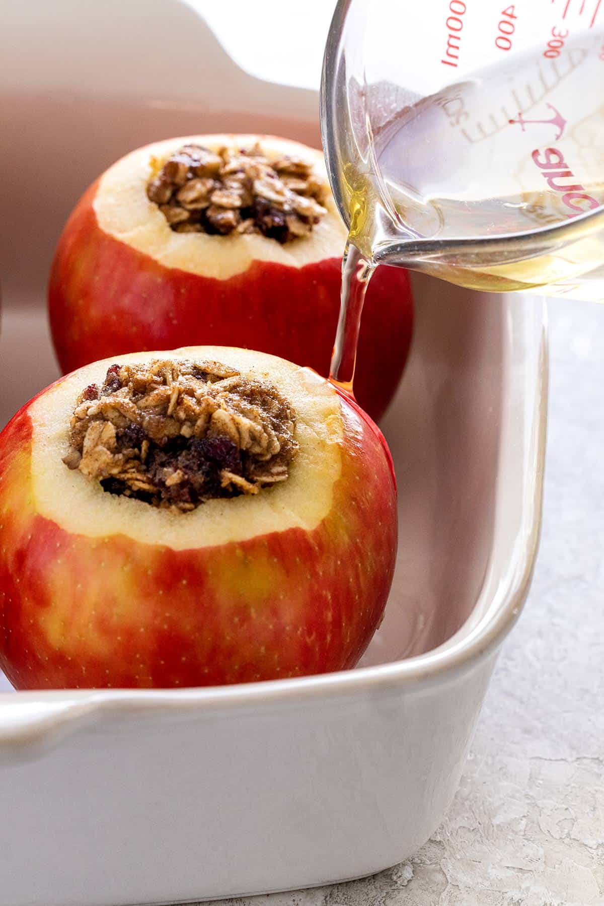 Two apples filled with oats in a white oven safe baking dish.