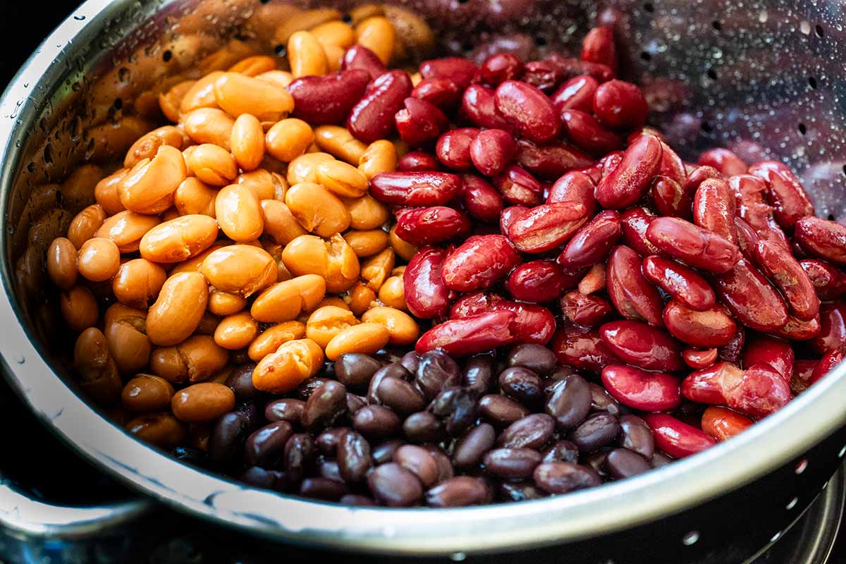 Three varieties of colorful beans being washed in a colander.