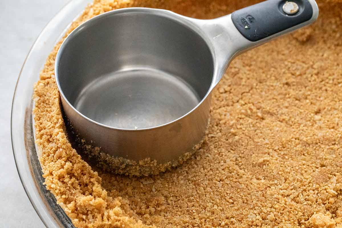 Flattening a pie crust in a glass plate with the back of a measuring cup.