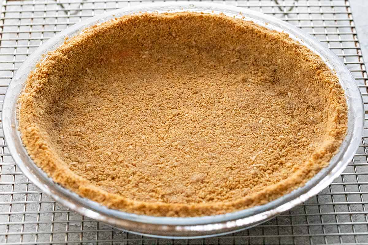 Baked graham cracker crust in a glass pie plate cooling on a wire rack.
