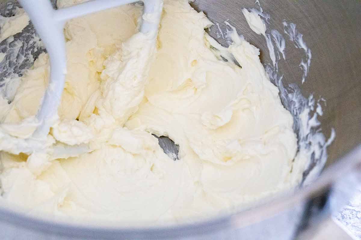 Soften cream cheese being whipped in the bowl of a stand mixer.