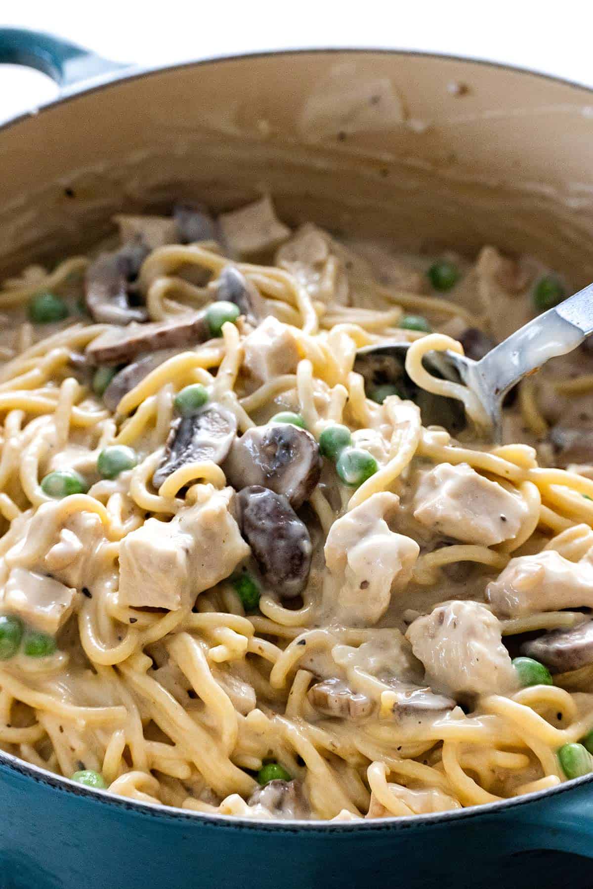 Mixing pieces turkey with spaghetti and cream sauce.