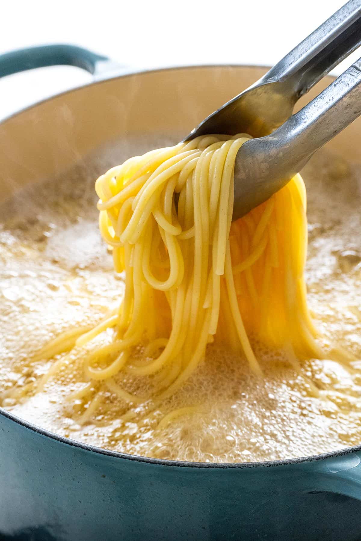 Lifting spaghetti out of boiling water with metal tongs.
