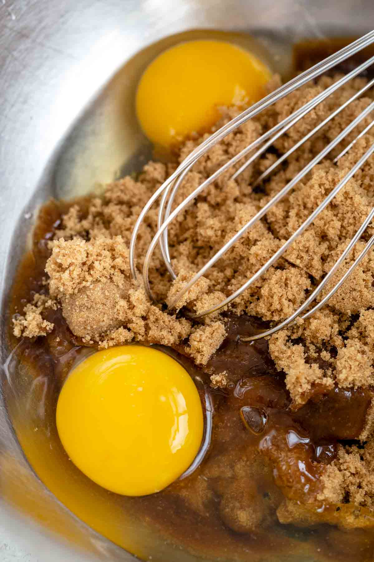 Brown sugar, eggs, and vanilla being whisked together in a metal bowl.