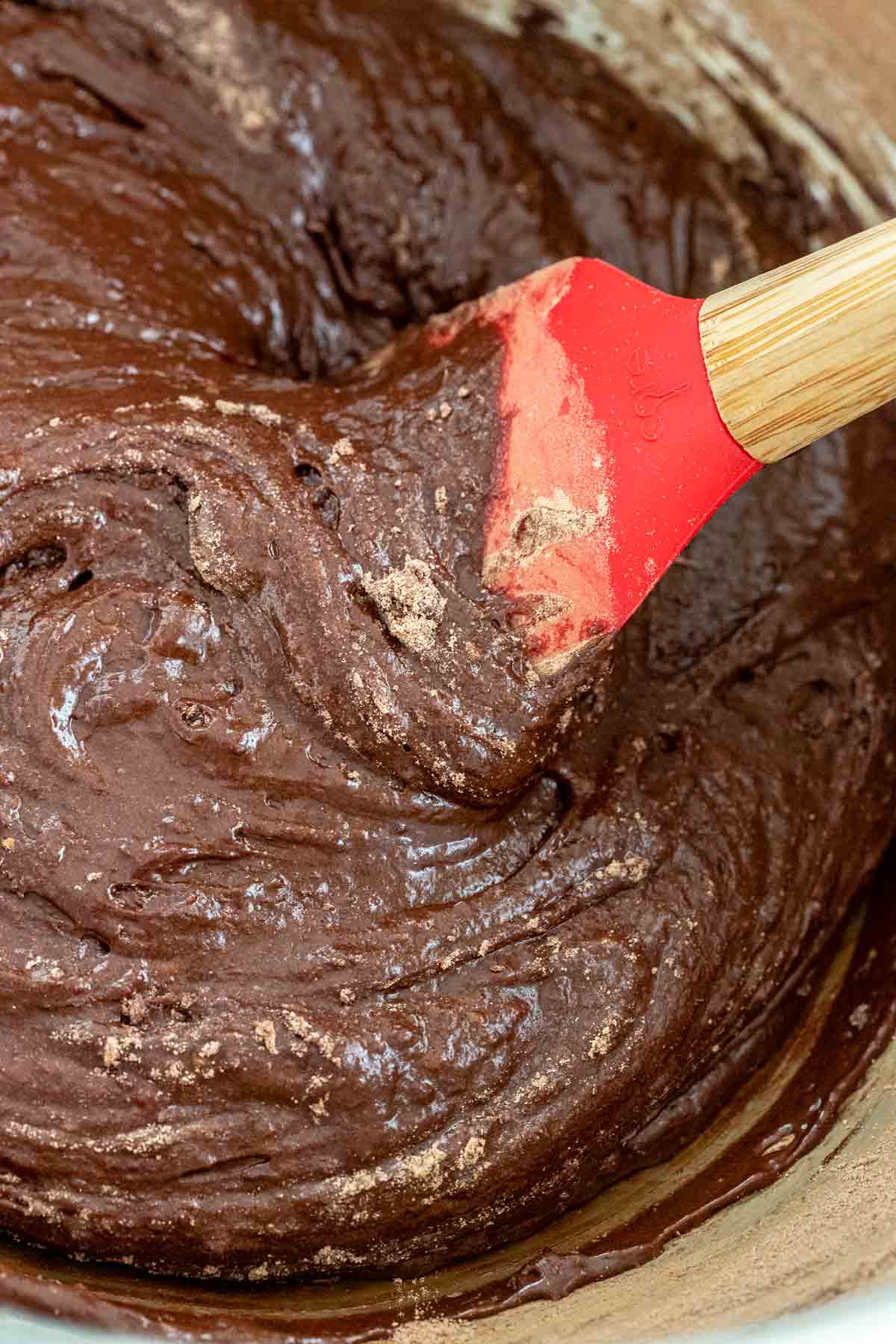 Thick chocolate cookie dough batter in a bowl being mixed with a spatula.
