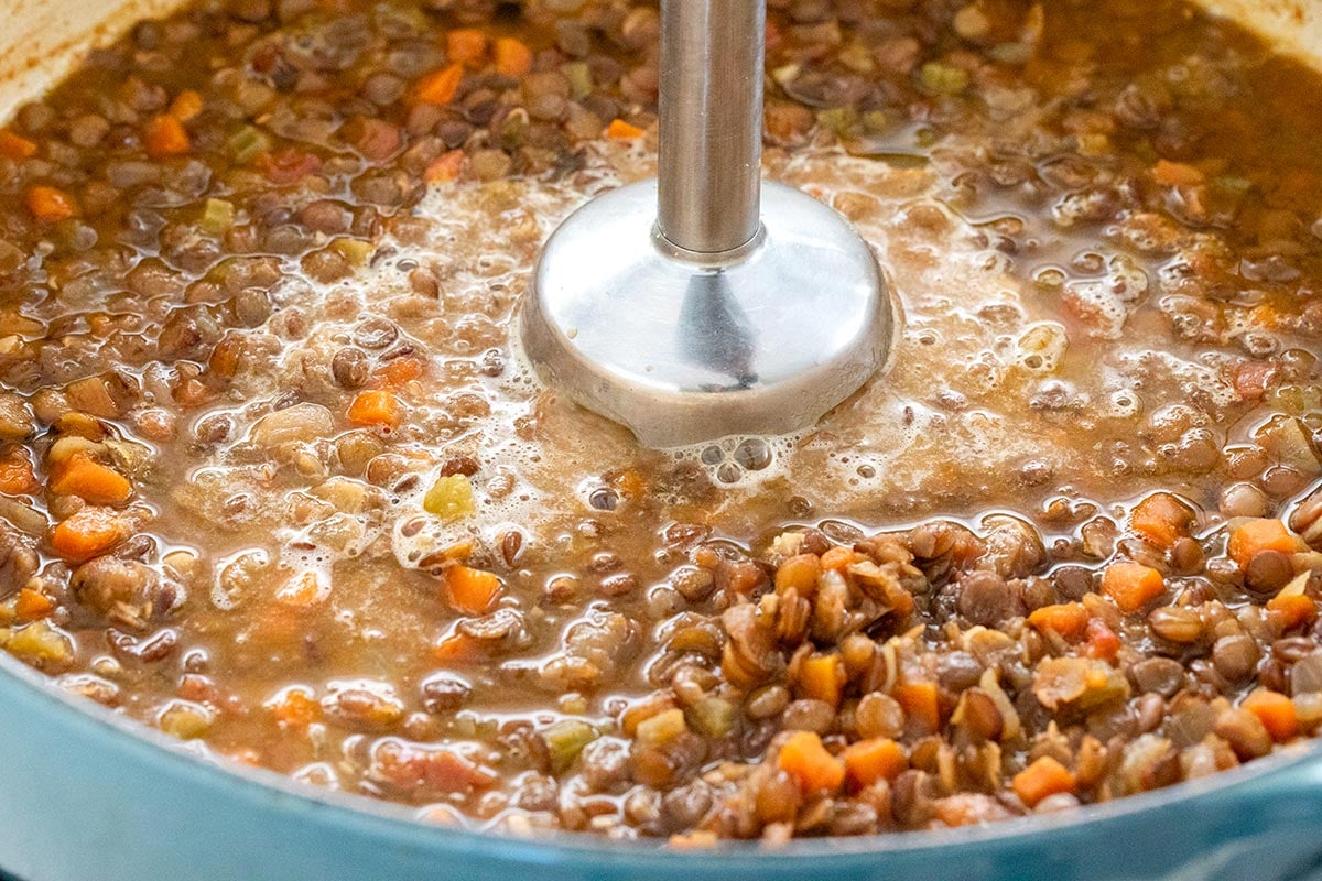 Hand immersion blender in a pot of lentil soup.