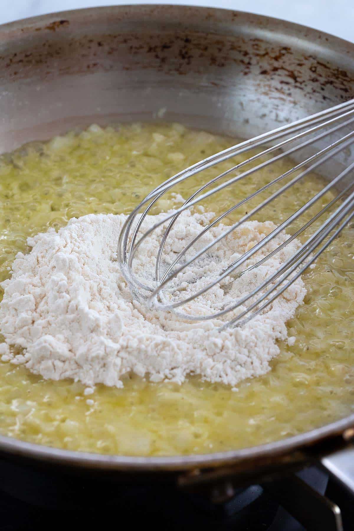 Incorporating flour into a pan with butter, onions, and garlic.