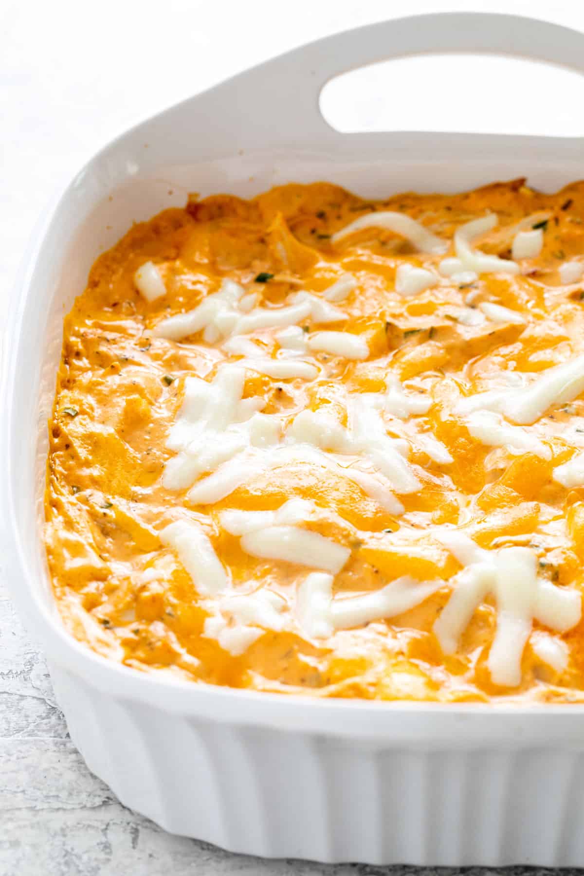 Melted shredded cheese on top of a baking dish filled with buffalo chicken dip.