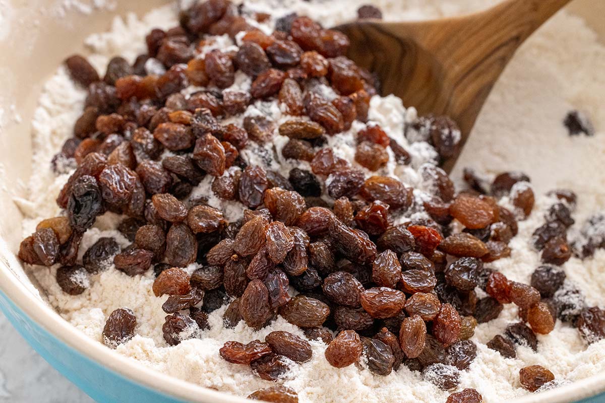 Raisins being mixed into a bowl of flour.