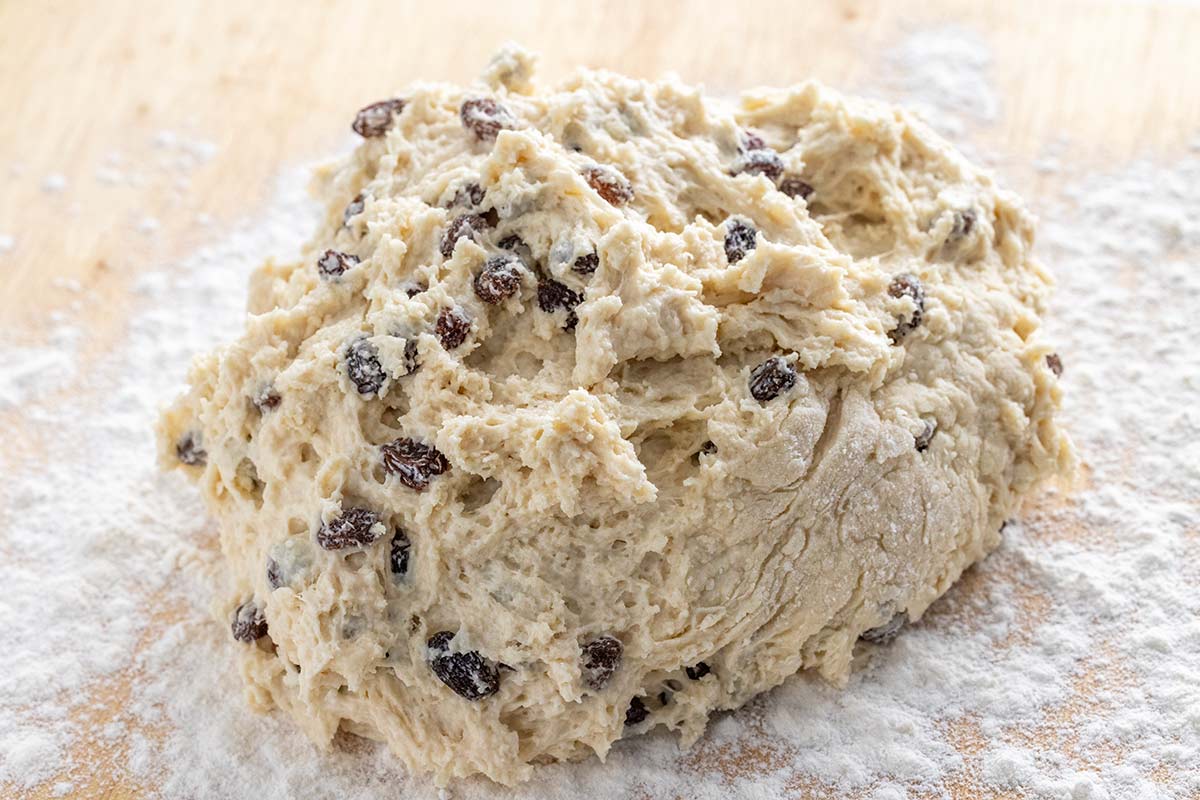 Soda bread dough with raisins being kneaded on a floured board.