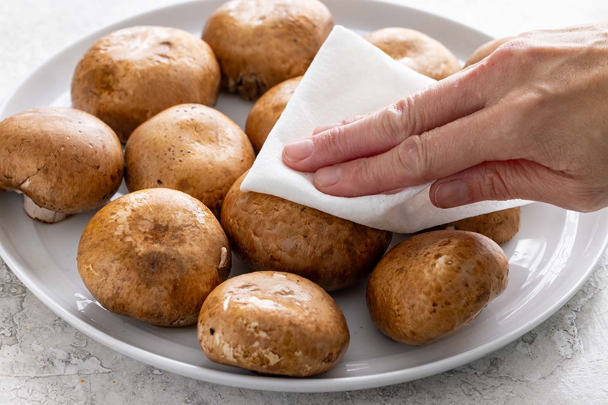 Person patting dry mushrooms using paper towels.