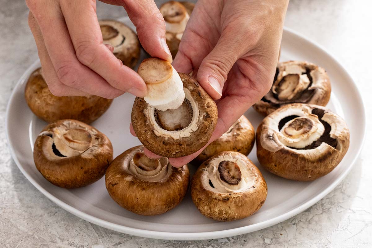 Person removing the stem from a mushroom using their fingers.