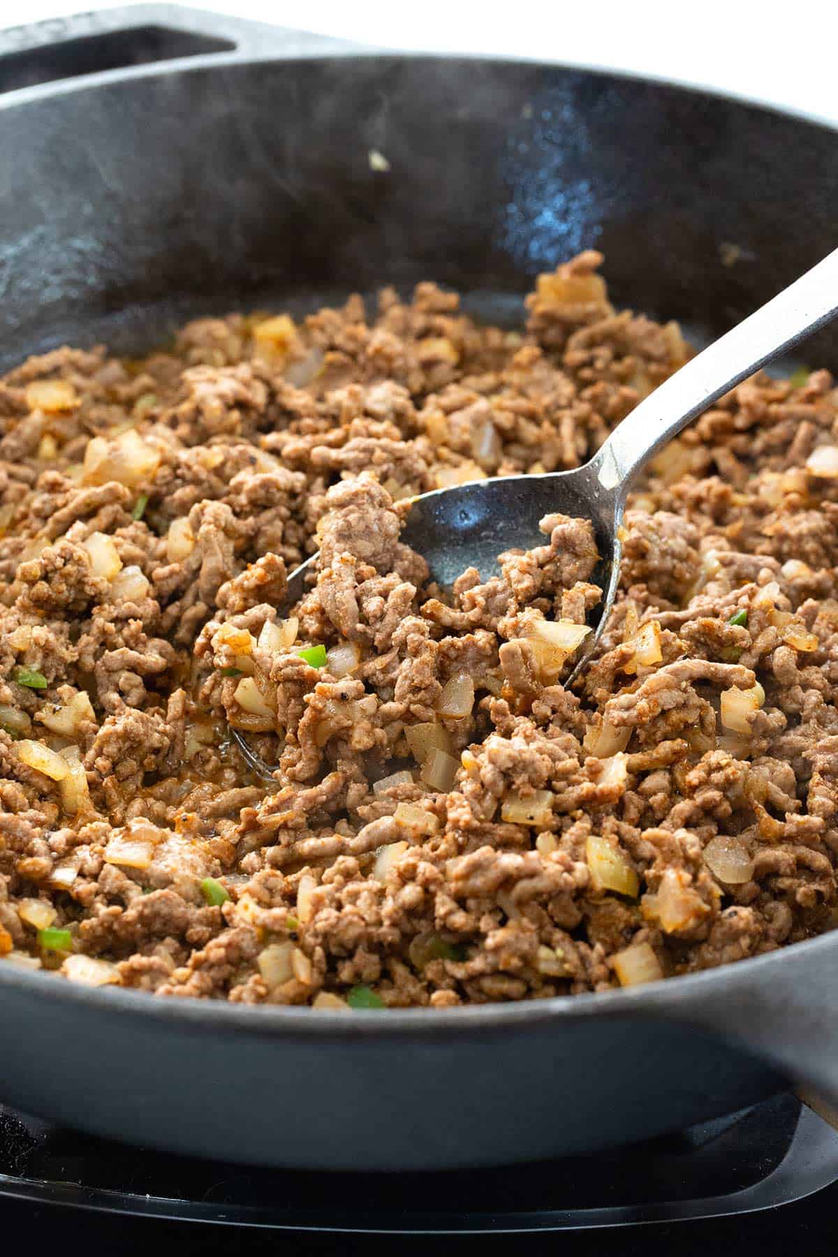 Ground beef mixture being cooked in a cast iron skillet.