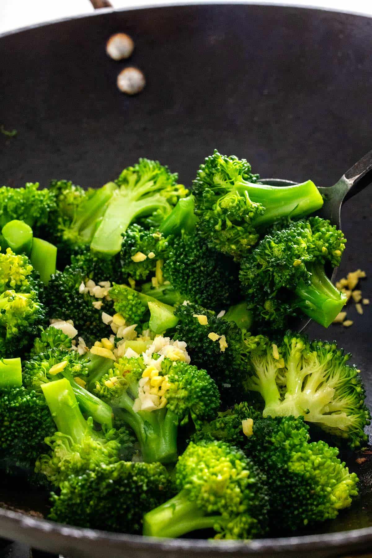 Bright green broccoli florets cooking in a wok with ginger and garlic.