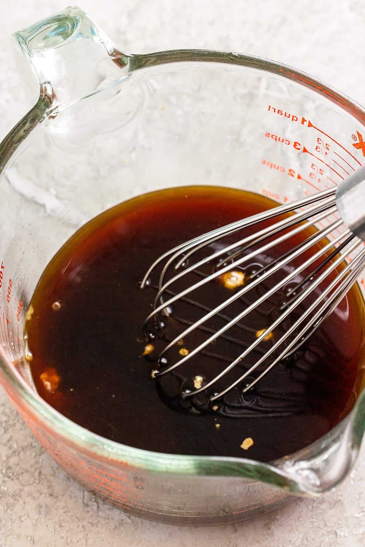 Whisk and stir fry sauce inside a clear glass measuring cup.