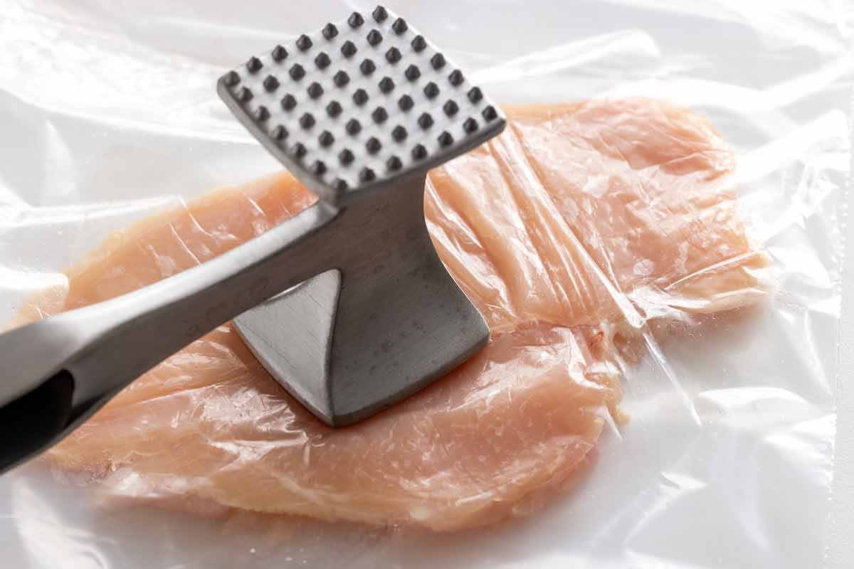 Chicken cutlet inside a plastic bag being flattened with a meat tenderizer.