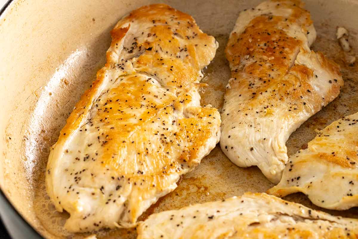 Seasoned chicken breasts with golden brown surface searing in a pan.