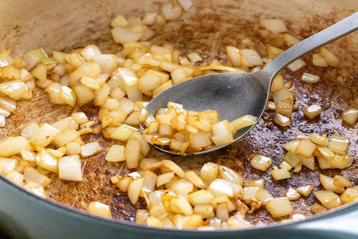 Sauteing pieces of onions and garlic in a large pan.