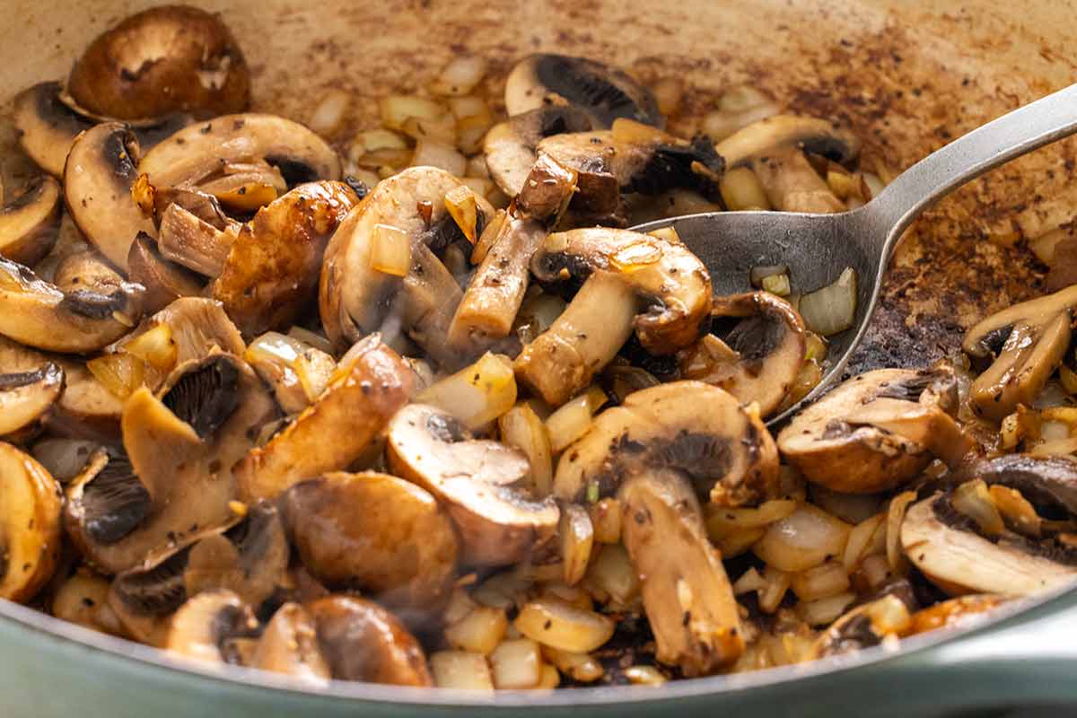 Sauteed brown mushrooms in a pan with pieces of onions and garlic.