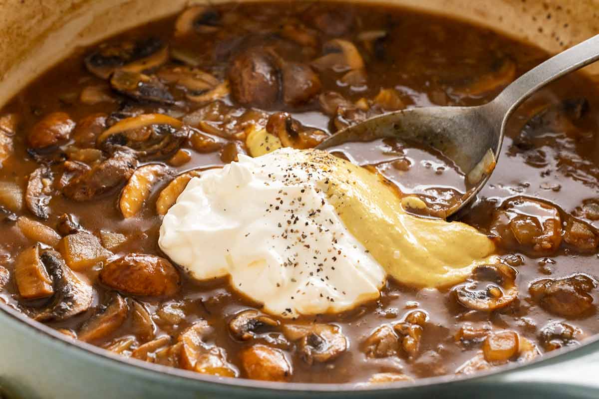 Sour cream and mustard added to a pan of mushroom sauce.
