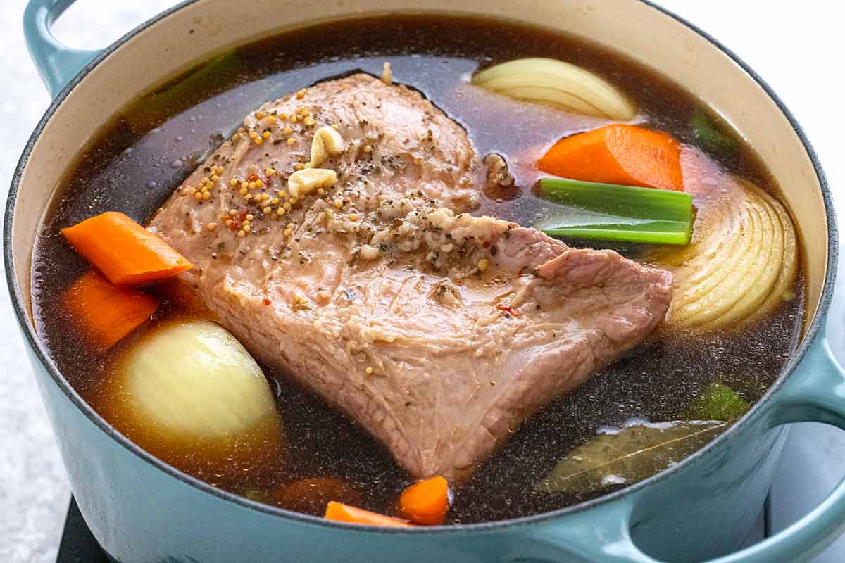 Cooked corned beef in a pot with carrots, potatoes, and onions.