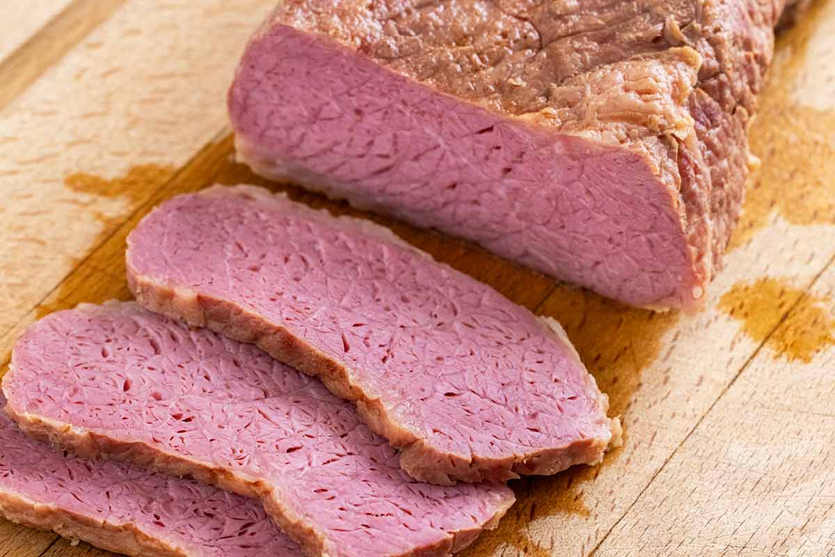 Corned beef cut into slices on a wooden cutting board.