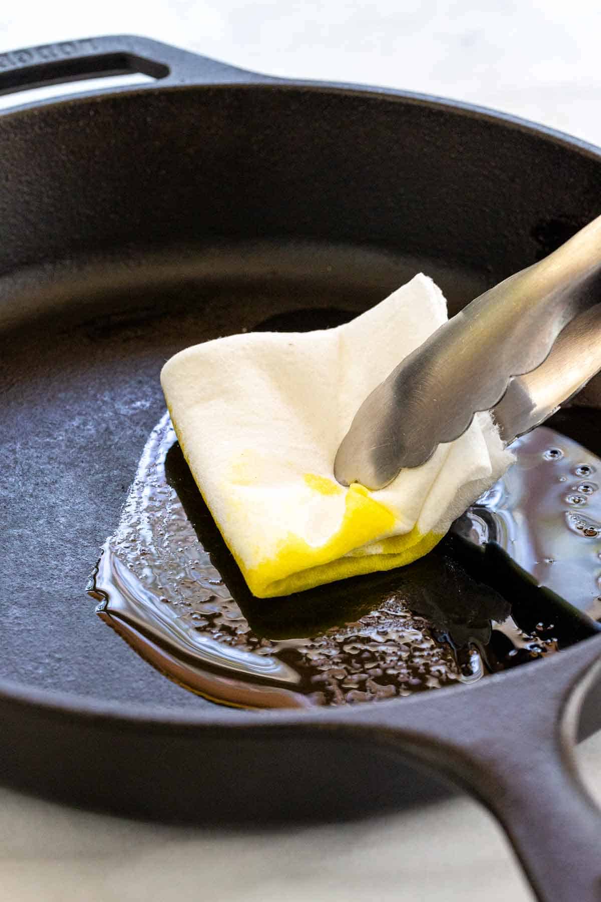 Using metal tongs and a paper towel to spread oil around in a hot pan.